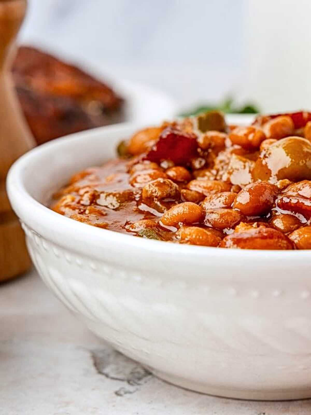 Close-up of a white bowl filled with baked beans in a thick, savory sauce.