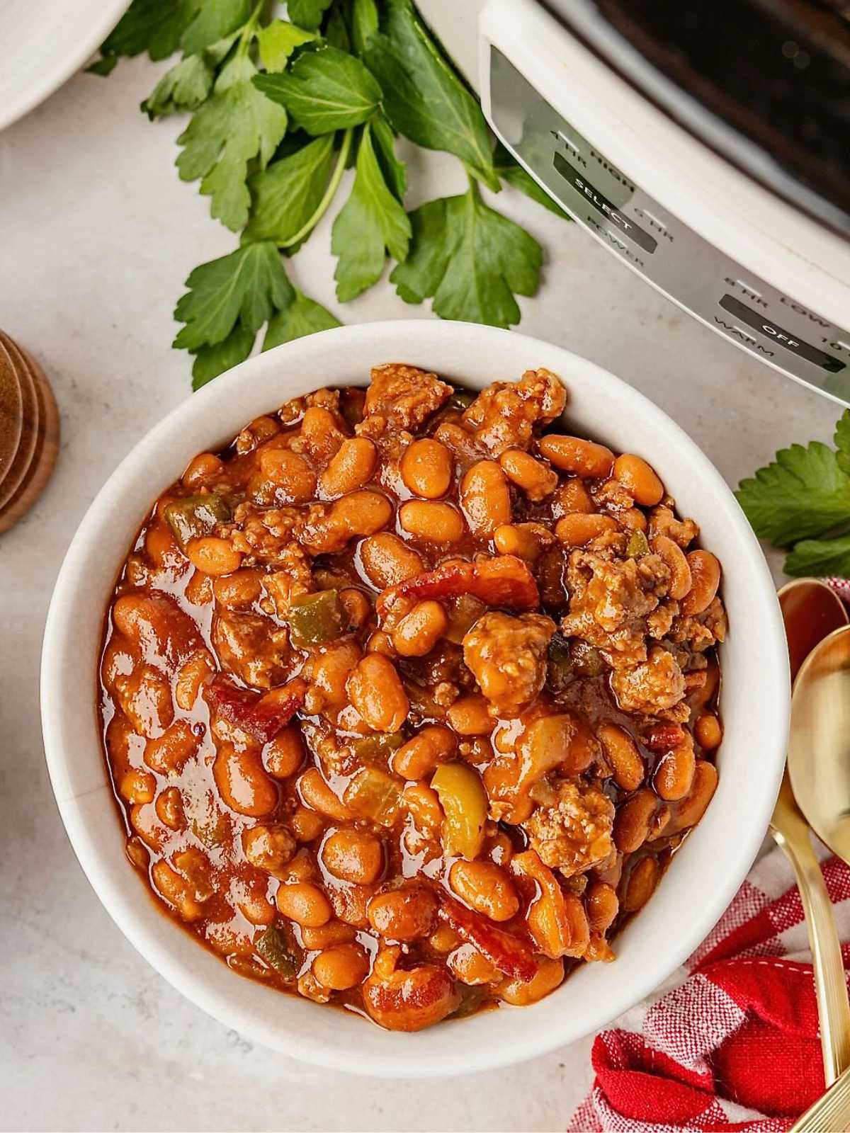 A white bowl filled with baked beans and ground meat, garnished with fresh parsley on the side.