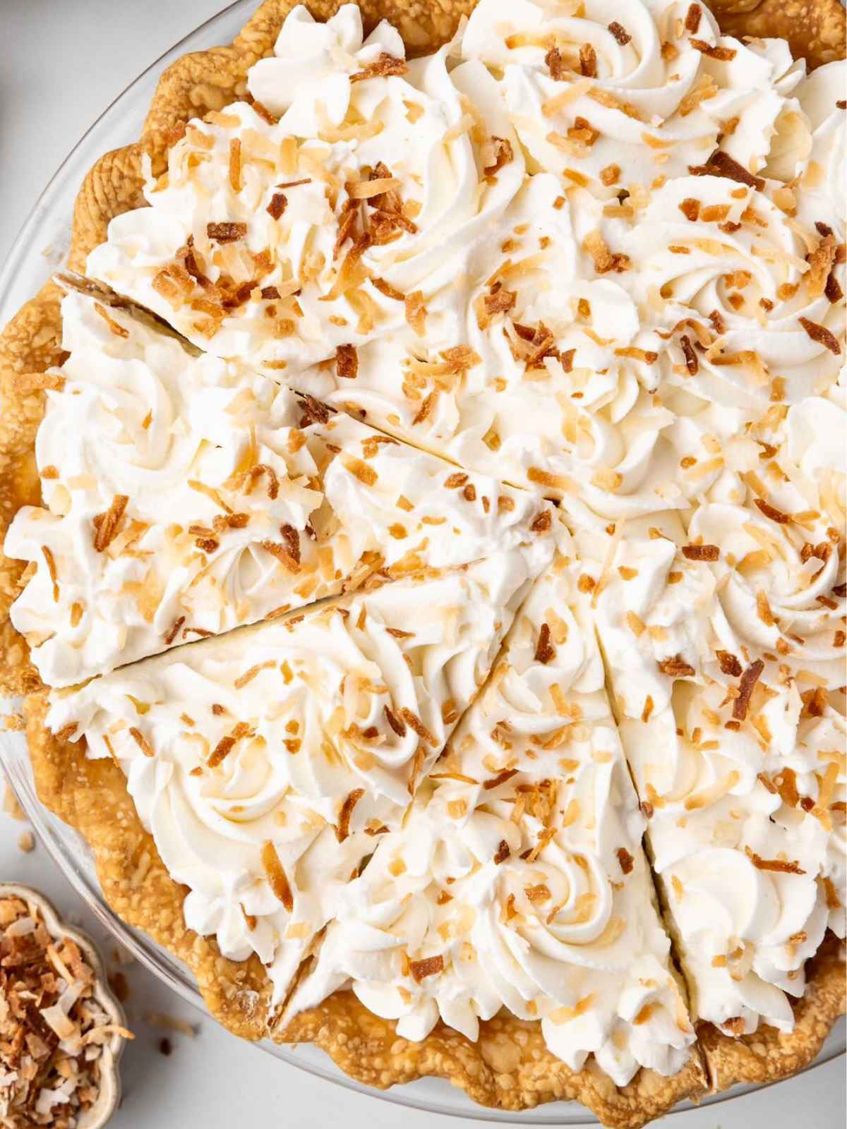 Coconut cream pie topped with whipped cream and toasted coconut, with a few slices cut.