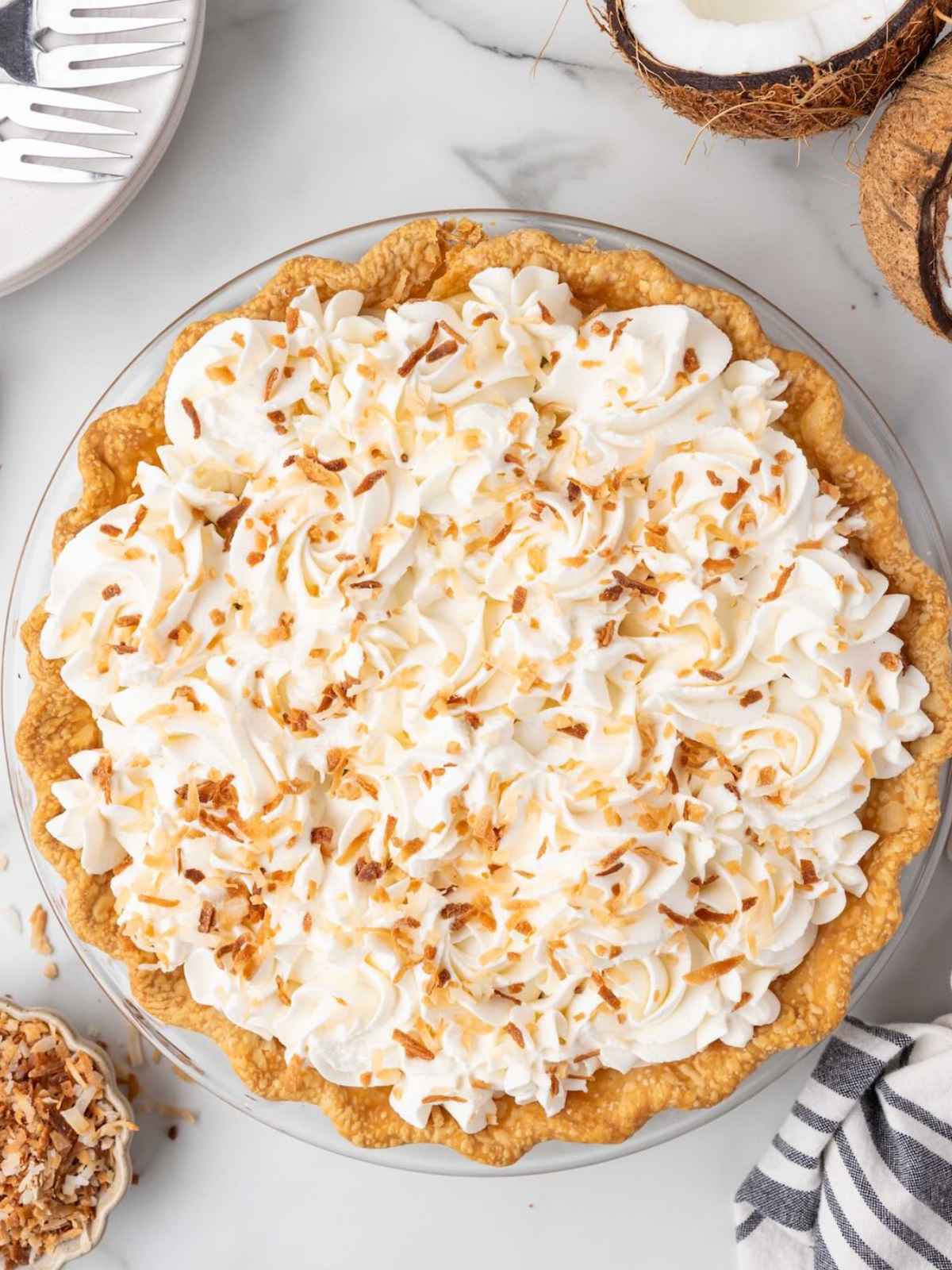 Coconut cream pie topped with whipped cream and toasted coconut on a marble surface.
