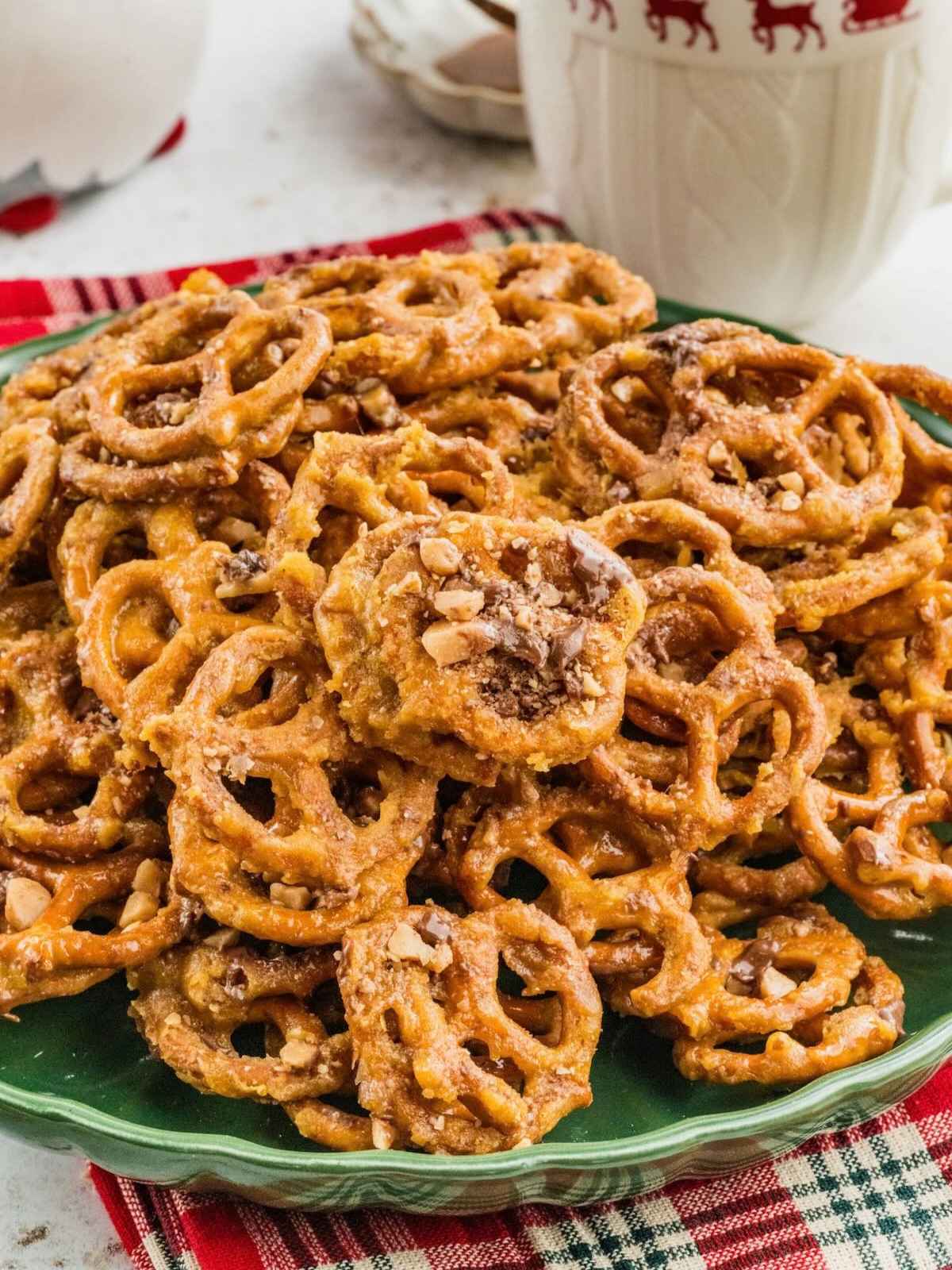 A green plate piled high with glazed pretzels topped with chopped toffee.