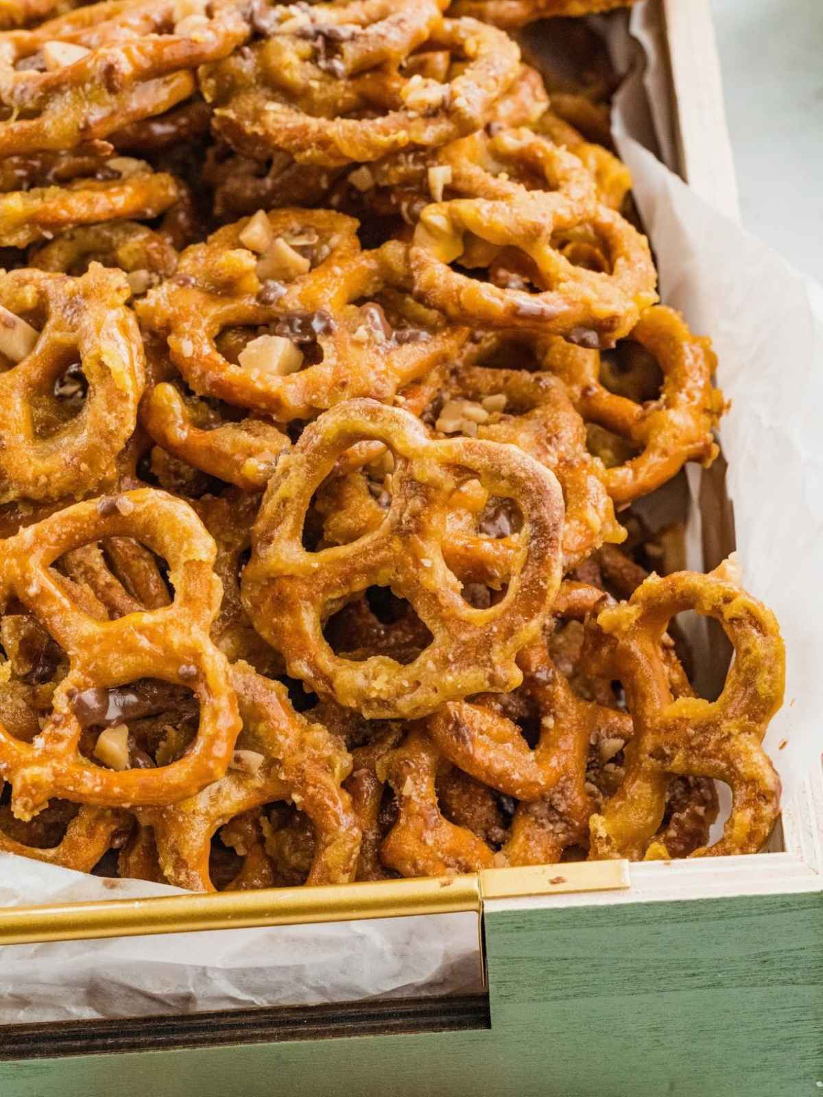A pile of glazed, chopped toffee-covered pretzels in a wooden crate lined with parchment paper.