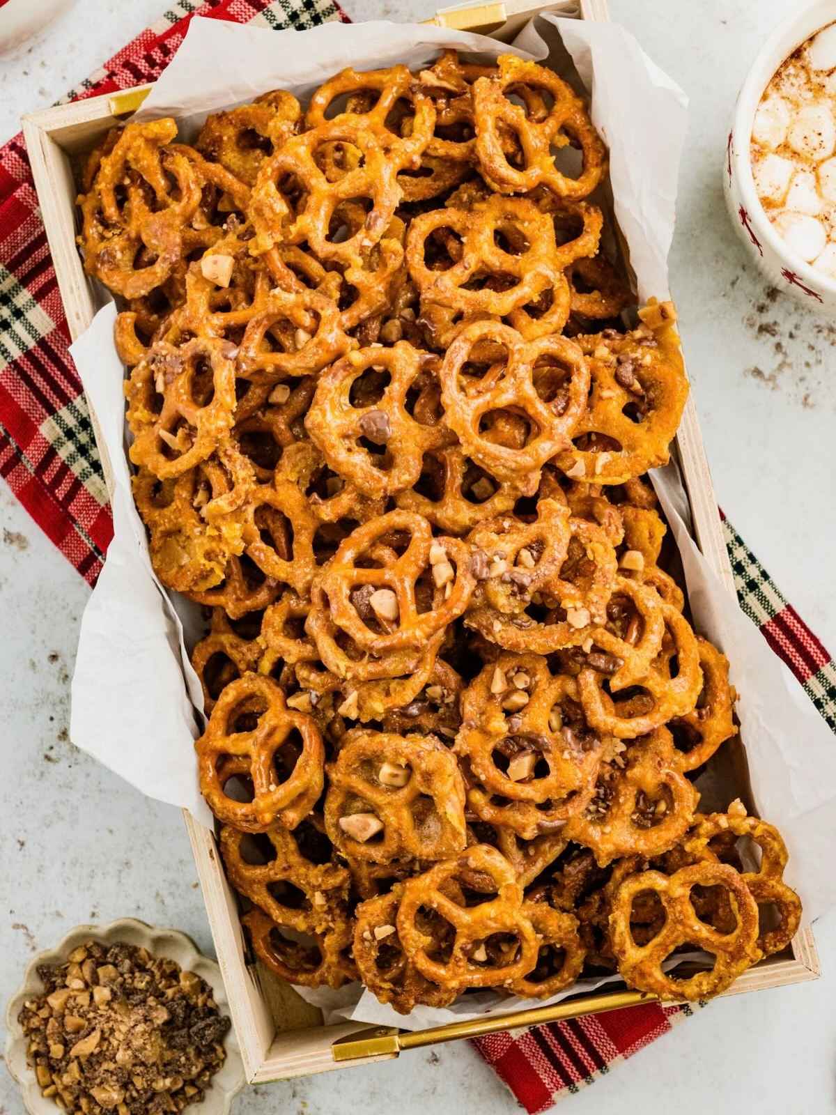 A wooden crate filled with caramel-coated pretzels topped with chopped toffee.