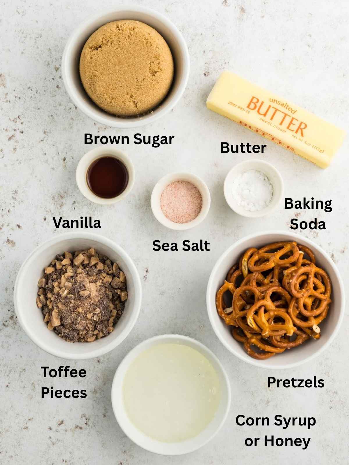 Ingredients for a recipe labeled brown sugar, butter, vanilla, sea salt, baking soda, toffee pieces, pretzels, and syrup.