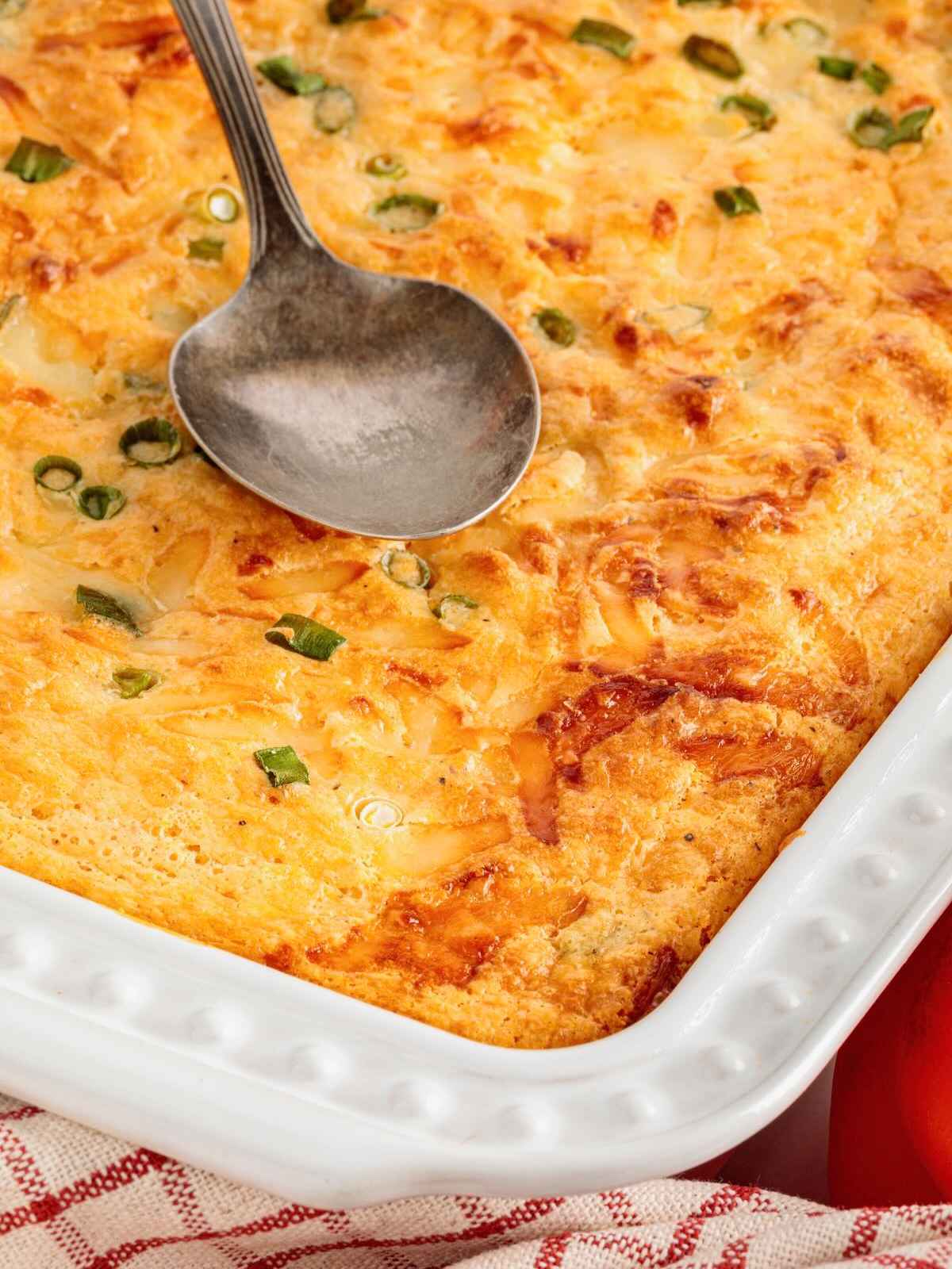 Baked cheese casserole topped with green onions and a metal serving spoon in a white baking dish.