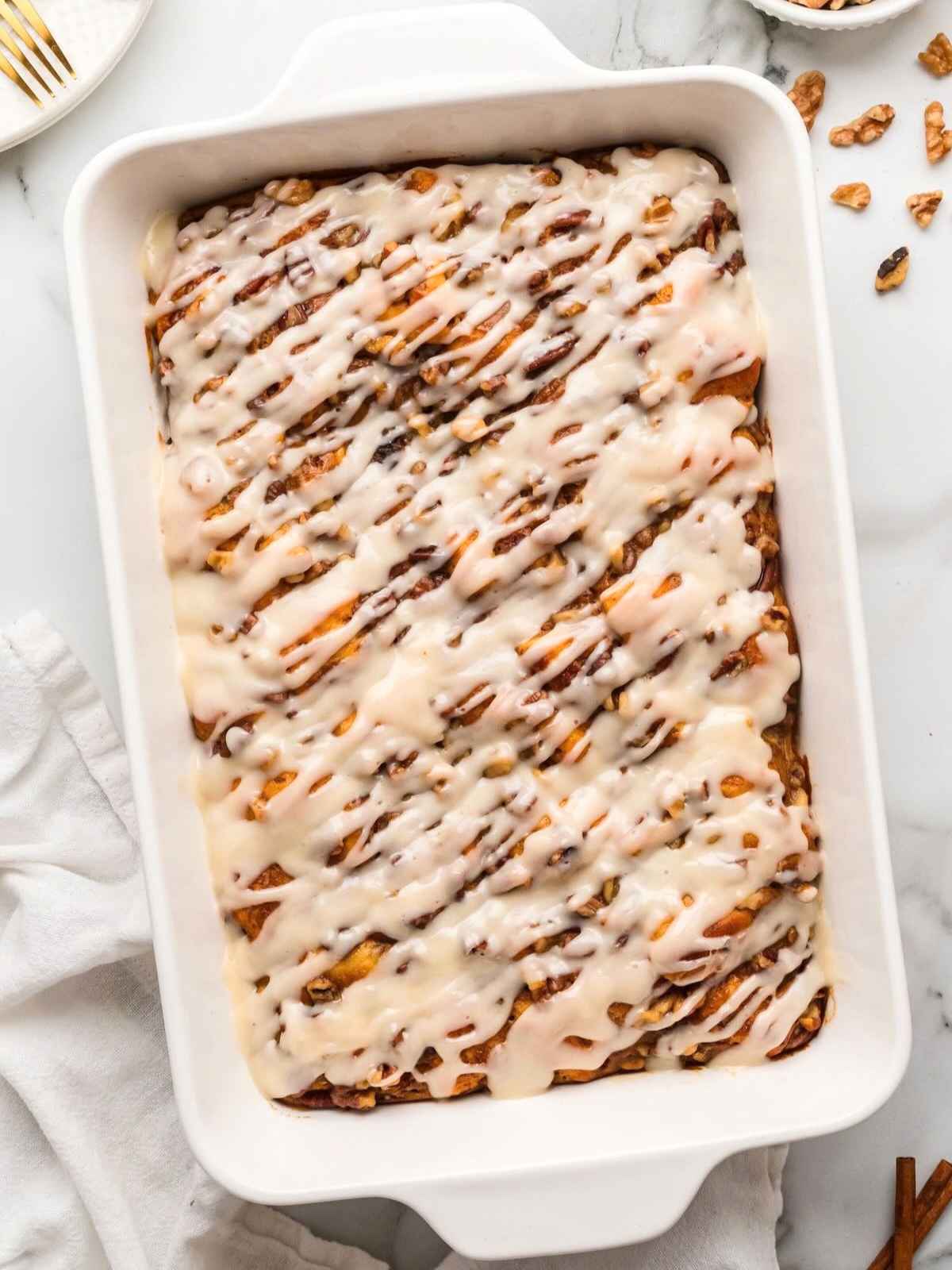 Rectangular pan of cinnamon rolls topped with white icing, viewed from above on a marble surface.