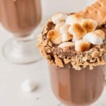Glass of hot chocolate topped with toasted marshmallows and a graham cracker rim.