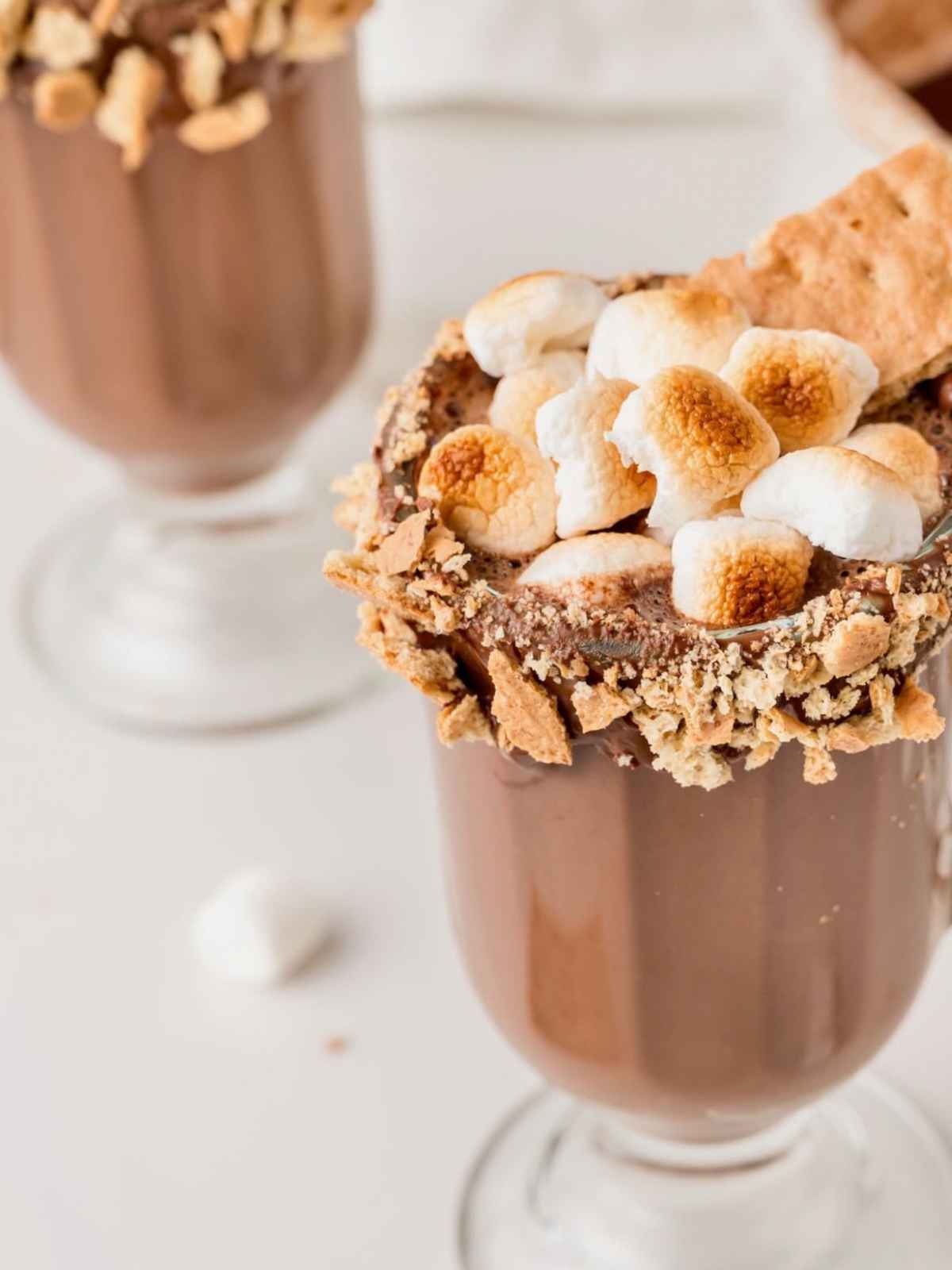 Glass of hot chocolate topped with toasted marshmallows and a graham cracker rim.