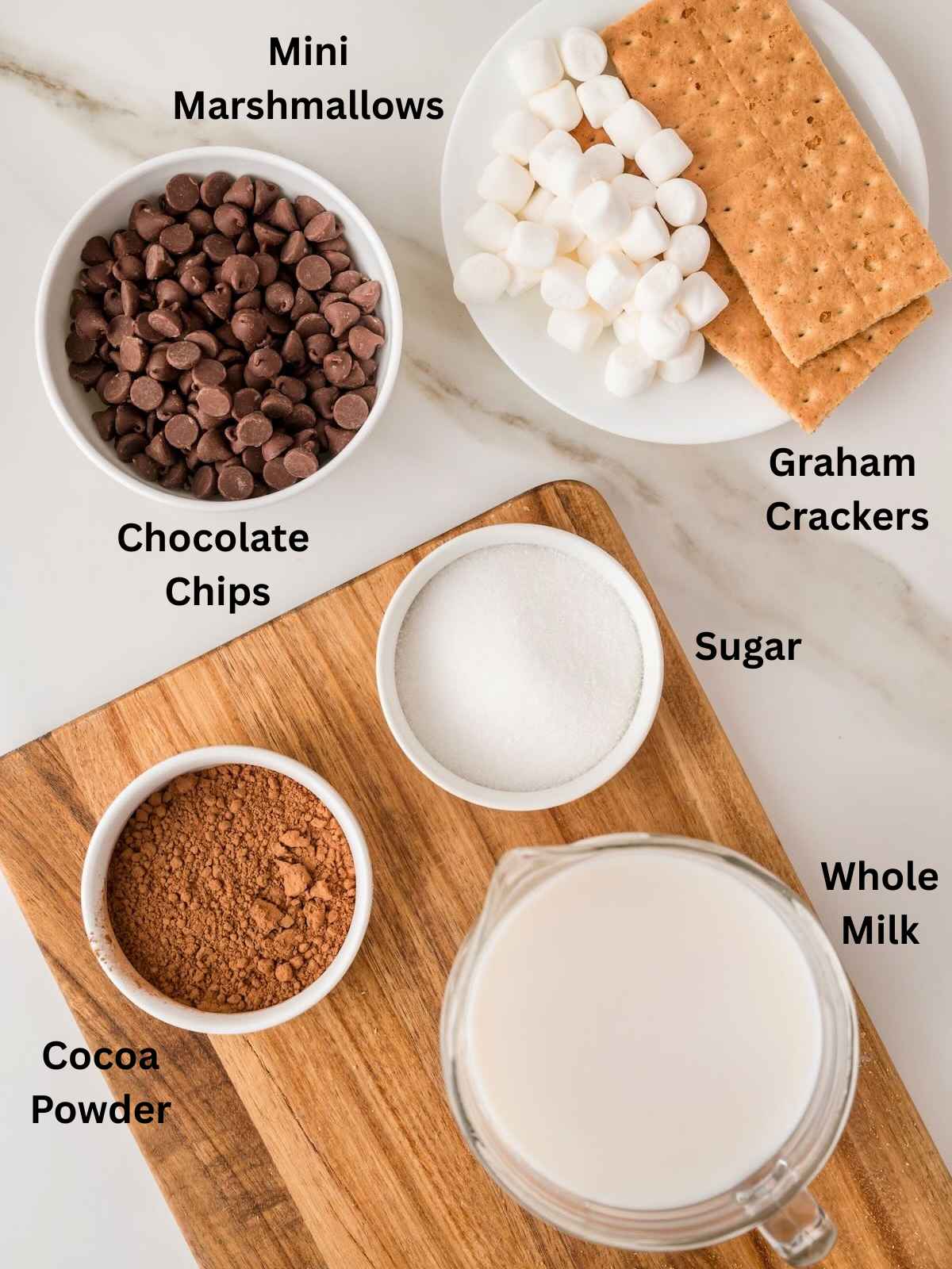 Ingredients for hot cocoa: mini marshmallows, graham crackers, chocolate chips, sugar, cocoa powder, and whole milk.